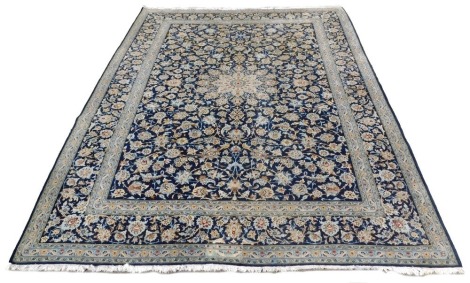 A Keshan blue ground rug, decorated with a central floral motif, with radiating flowers around, within repeating floral and foliate borders, 405cm x 312cm.