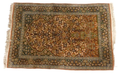 A Qum wool and silk mix orange ground prayer rug, the mihrab containing a vase with flowers emanating all over from it, within repeating floral borders, 197cm x 123cm.