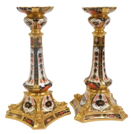 A pair of Royal Crown Derby porcelain candlesticks decorated in the Old Imari pattern, with shaped drip tray, tapering stem, on a shaped square base decorated with four dolphins, numbered 1128, red printed marks, 26cm high. (AF)