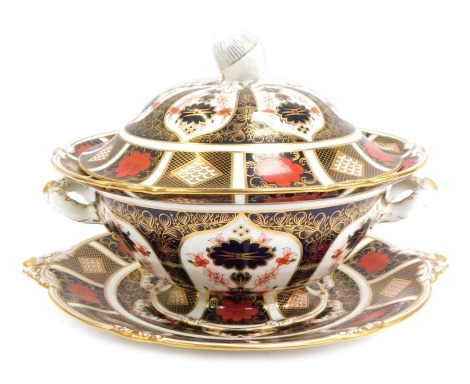 A Royal Crown Derby porcelain twin handled soup tureen and cover decorated in the Old Imari pattern, the lid with acorn finial, with a circular dish, on an out swept circular base, number 1128, 25cm high, together with a twin handled platter, each handle 