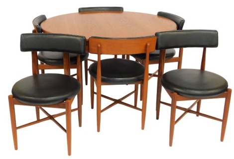 A G-Plan teak dining table and chairs, the dining table with a circular top, on cylindrical tapering legs, 74cm high, the top 122cm diameter, together with a set of six chairs, each with a padded black leatherette back and circular seat, on cylindrical ta