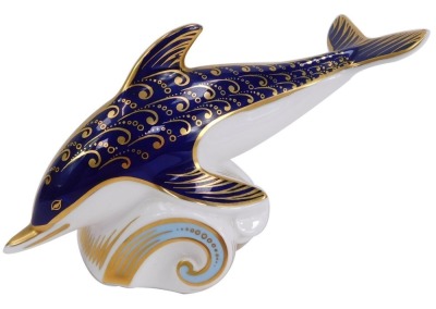 A Royal Crown Derby porcelain paperweight modelled as a dolphin riding a wave, gold stopper and red printed marks, 10cm high.