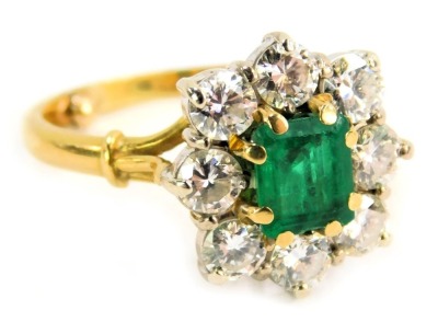 An emerald and diamond cluster ring, the rectangular cut emerald, approx 0.50ct, in eight claw setting surrounded by eight round brilliant cut diamonds, each approx 0.10ct, on a raised white gold basket setting, on yellow metal band with dot adjusters, ye