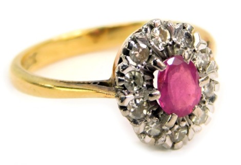 A ruby and diamond cluster ring, the central oval ruby in a six claw setting, approx 0.25ct, surrounded by ten round brilliant cut diamonds, each illusion set, approx 0.02ct, in platinum on a yellow metal band stamped 18ct, ring size P, 4.5g all in.