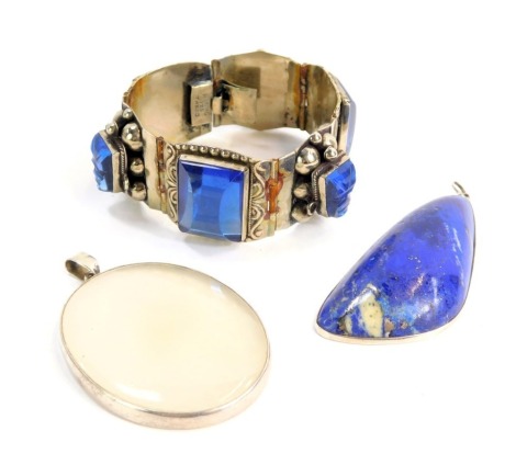 Eastern inspired jewellery, comprising a lapis lazuli pendant, in a rub over white metal finish border, 7cm high, a moonstone type pendant in a white metal frame, stamped 925, 6cm high, and a blue paste stone set hinged bracelet, marked Taxco, white metal