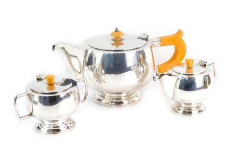 An Art Deco three-piece tea set, comprising a teapot, a lidded milk jug and a sucrier, with orange Bakelite knops and handle to teapot, white metal stamped Silver, the teapot 14cm high. 32.84oz.