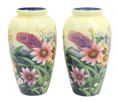 A pair of Old Tupton Ware pottery vases, each tube line decorated with flowers, including sunflowers, daisies, etc., against a pale yellow ground, printed marks, 28.5cm high.