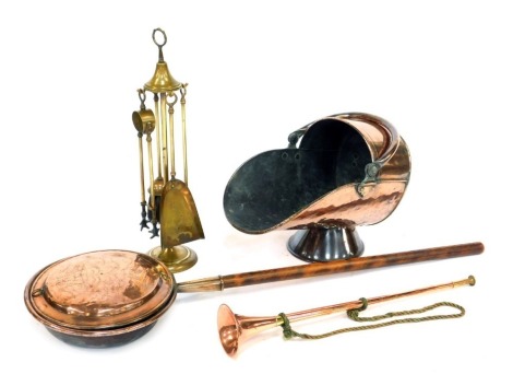 Assorted copper and brass wares, comprising a brass fireside companion set, 55cm high, a copper hunting horn, 62cm long, a copper warming pan with turned wooden handle, 125cm long, and a copper helmet shaped coal scuttle, 45cm wide. (4)