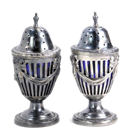 A pair of Edward VII silver Adam style pepperettes, pierced baluster form, embossed with bow tied swags, and blue glass liners, Walker & Hall, Sheffield 1905, 4.27oz gross (including a stuck liner). (AF)