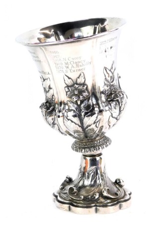 A Victorian vase, with embossed floral decoration, raised on a leaf and C scroll embossed shaped base, later engraved as a trophy, white metal, 17.19oz, 22cm high. (AF)