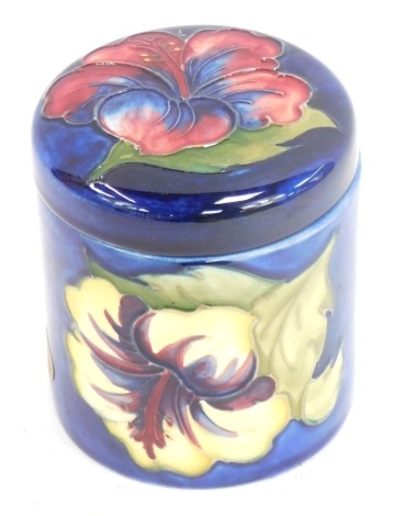 A Moorcroft pottery Hibiscus pattern jar and cover, of cylindrical form, blue ground, impressed marks and paper labels, 10cm high.