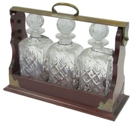 A 20thC Piers Hart mahogany and brass bound Tantalus, with three cut glass decanters and stoppers, and silver decanter labels for Port, Brandy, and Whisky, Birmingham 1919, 32cm high, 41cm wide, 16cm deep.