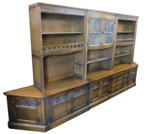 An Old Charm oak lounge unit, the top with an arrangement of leaded glazed doors, shelves, etc., above an arrangement of carved panelled doors and drawers to base, on plinth, in four sections, 184cm high, approx 350cm wide, 55cm deep.