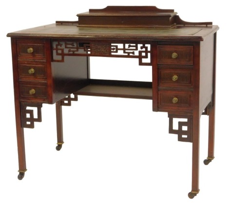 A late Victorian mahogany Aesthetic influence desk, the rectangular top with a gilt tooled leather inset and raised hinged recess for pens, the base with an arrangement of six small drawers and pierced fretwork on square legs with castors, 78cm high, 92cm