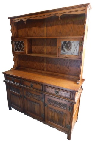 An Old Charm oak dresser, the moulded top above an arrangement of shelves and two leaded glazed cabinets, the base with three drawers above three carved cupboards, on stiles, 174cm high, 135cm wide, 44cm deep.