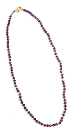 A 20thC garnet faceted necklace, on a knotted silk strand, yellow metal clasp, unmarked, 40cm long, 11.7g all in.