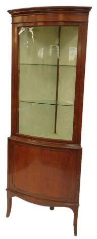 An Edwardian mahogany standing corner cabinet, the top with a moulded edge above a glazed door enclosing two glass shelves, the base with a panelled door enclosing shelf, on out swept legs, 182cm high, 67cm wide, 41cm deep.