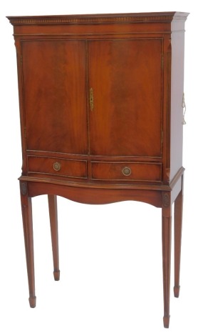 A 20thC mahogany cocktail cabinet, the top with a dentil moulded edge above two doors enclosing a mirror back interior, with two shelves and sliding drawer, the base with two frieze drawers with curved apron and floral roundels, on splayed legs, 156cm hig