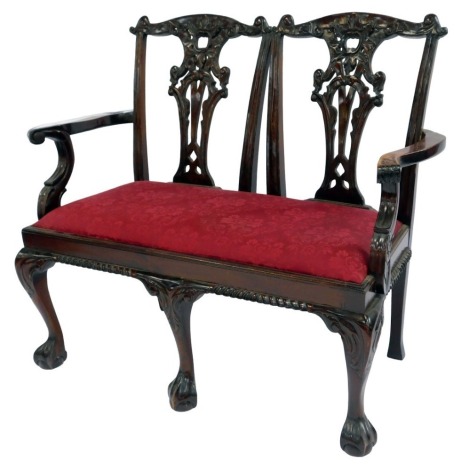 A reproduction mahogany Chippendale style two seater settee, each carved back with scrolling arms, drop in seat upholstered in red foliate fabric, raised on ball and claw feet, 113cm wide.