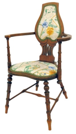 An Edwardian mahogany bedroom chair, the shaped and pierced back with overstuffed floral upholstery with scrolling arms, on a kidney shaped upholstered seat, on turned cylindrical legs.