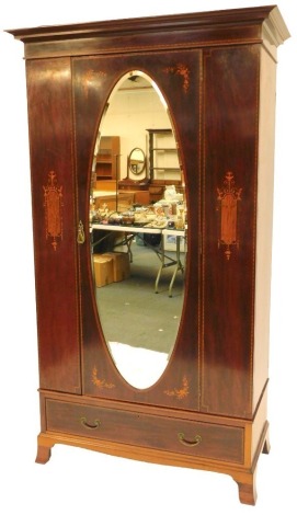 An Edwardian mahogany and inlaid wardrobe, the top with a moulded cornice above an oval bevelled mirror door, enclosing hanging rail and hooks, the front with inlaid decoration with urns, flowers, scrolls, etc., with drawer to base, on bracket feet, 210cm