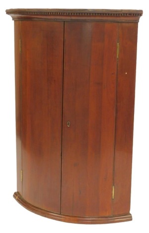 A 19thC mahogany bow fronted corner cabinet, the top with a dentil moulded edge above two doors enclosing shelves, 113cm high, 79cm wide, 55cm deep.