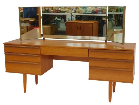 A mid century teak mirror back dressing table, the base with an arrangement of seven drawers, on rounded triangular feet, 113cm high, 160cm wide, 44cm deep.