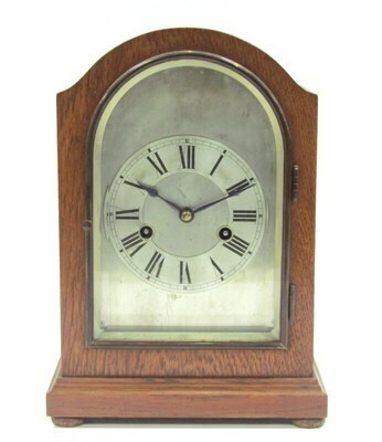 A 20thC oak cased mantel clock, the arched and domed top above a silvered backplate and dial, with Roman numerals, on bun feet with black handles, 28cm high, 20cm wide, 13cm deep.