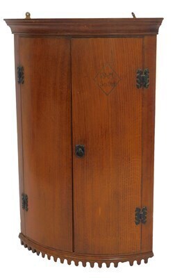 An early 20thC oak bow fronted corner cabinet, the top with a moulded edge above two doors, one carved Ram Sep 1924, with a shaped carved section to base, 99cm high, 66cm wide, 44.5cm deep.