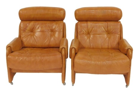 A pair of 1970s brown leather armchairs, each with a headrest, buttoned back and seat, on castors, 74cm wide. The upholstery in this lot does not comply with the 1988 (Fire & Fire Furnishing) Regulations, unless sold to a known exporter or upholsterer it 