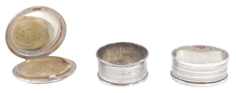 Three items of silver, comprising a George V silver powder compact, with engine turned decoration of circular form, makers C&A Birmingham 1905, with brass cover, and two silver napkin rings, 2oz.. (3)