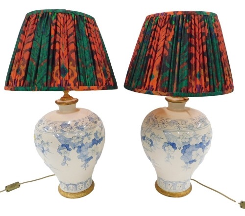 A pair of Chinese style baluster shaped table lamps, each ceramic body with a design of flowers and leaves, and with a multicoloured shade, 70cm high.