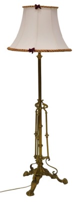 An early 20thC brass floor lamp, decorated in Art Nouveau style with patera, tapering feet, converted to an oil lamp, 150cm high including shade.