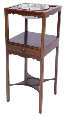 A George III mahogany washstand, the square top with a recess for a bowl and two further beaker recesses, above a second tier with drawer, on square section legs with concave stretcher, the recess now with associated ironstone bowl, 79cm high, 32cm wide.