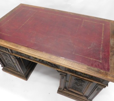 A Continental carved kneehole oak desk, the rectangular top with an ox blood red leatherette inset, with a moulded edge above arrangement of three frieze drawers and two panelled doors, on plinth, 83cm high, 153cm wide, 92cm deep. (AF) - 2