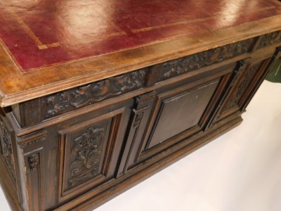 A Continental carved kneehole oak desk, the rectangular top with an ox blood red leatherette inset, with a moulded edge above arrangement of three frieze drawers and two panelled doors, on plinth, 83cm high, 153cm wide, 92cm deep. (AF) - 6