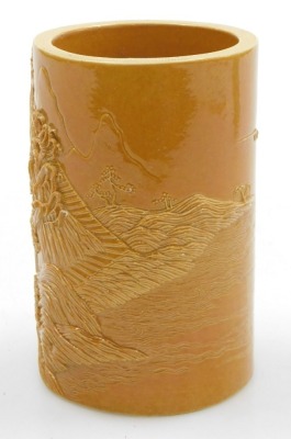 An ochre glazed porcelain brush pot, of cylindrical form, carved in relief with seated buddha in a river landscape, four character Qianlong seal mark, 12.5cm high. - 2