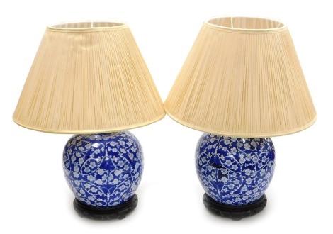 A pair of 20thC Chinese blue and white porcelain table lamps, of bulbous form with covers, decorated with prunus blossom, within butterfly shaped tendrils on wooden stands, converted to lamps, 46cm high.