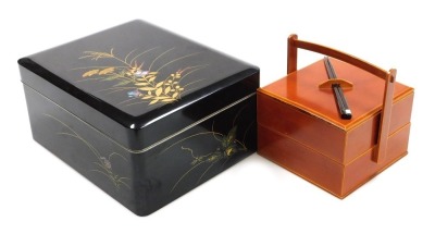 A Japanese black lacquer box and cover, decorated with grasses and flowers, together with a brown lacquer bento box, of two section form, with lid holding a pair of chopsticks, 17.5cm high, 17cm wide, 16.5cm deep. (2)