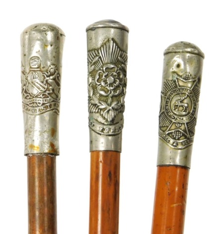 Three British Army malacca cane swagger sticks, with regimental crested terminals, for the Manchester Regiment, East Yorkshire Regiment, and the Bedfordshire and Hertfordshire Regiment.