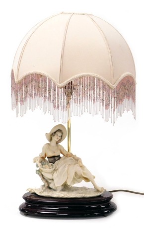 A Giuseppe Armani Capodimonte figural table lamp, modelled as a seated lady with a bowl of fruit, raised on an oval wooden stand, with shade, 59cm high.