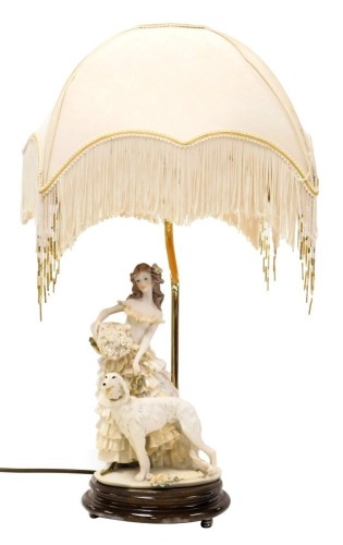 An A Belcari figural table lamp, modelled as a lady in a crinoline dress, holding a basket of roses aside an Afghan hound, raised on a wooden base, with shade, 56cm high. Buyer Note: WARNING! This lot contains untested or unsafe electrical items. It is su