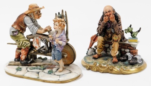 A Capodimonte figure group, modelled as a knife grinder with boy, raised on a naturalistic oval base, 31cm wide, and a further figure of a tramp seated upon a bench, possibly titled Bookworm, on an oval naturalistic base, 25cm wide. (2)(AF)