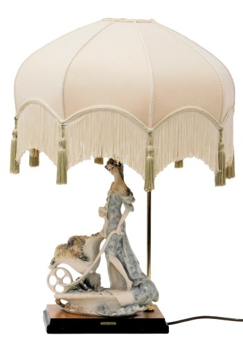 A Giuseppe Armani Capodimonte figural table lamp, modelled as a lady pushing a barrow of flowers, raised on a wooden base, with shade, 64cm high.