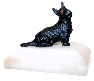 An Art Deco style cold painted metal figure of a Scottie dog, modelled in seated pose, on a white onyx base, 8.5cm wide.