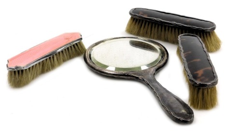 A George V silver and tortoiseshell backed three piece dressing table set, comprising a hand mirror and pair of clothes brushes, Birmingham 1918, together with a chrome and pink guilloche enamel clothes brush. (4)