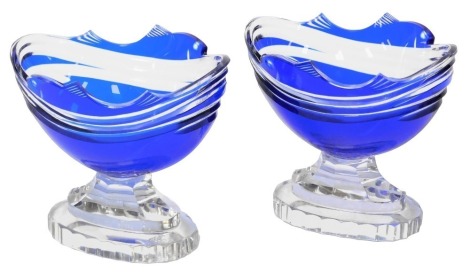 A pair of early 20thC blue glass sweetmeat dishes, carved to the rims with fish amongst waves, on a faceted outswept tiered oval base, 13.5cm wide.