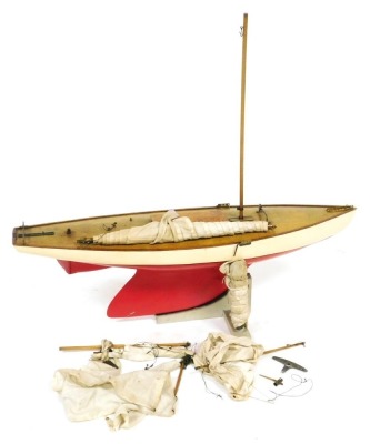 An early 20thC wooden pond yacht, with a cream and red painted hull, with rigging and sails, 90cm wide.