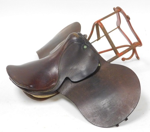 An early 20thC brown leather saddle, together with an early 20thC red painted wrought iron saddle rack, 51cm high. (2)