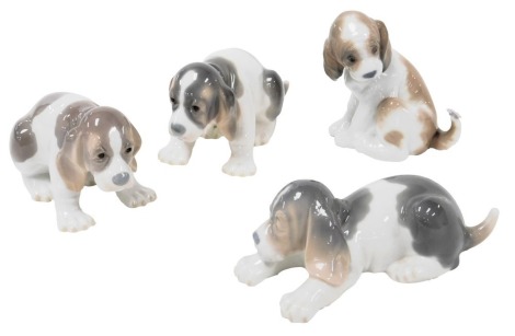 Four Lladro porcelain figures of spaniel puppies, one with a butterfly on its tail.